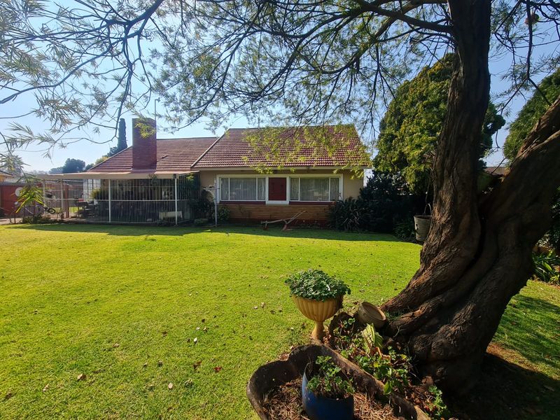 A view of the rear of the house featuring a large lawn, a covered patio area, and a tiled roof with a brick chimney.
