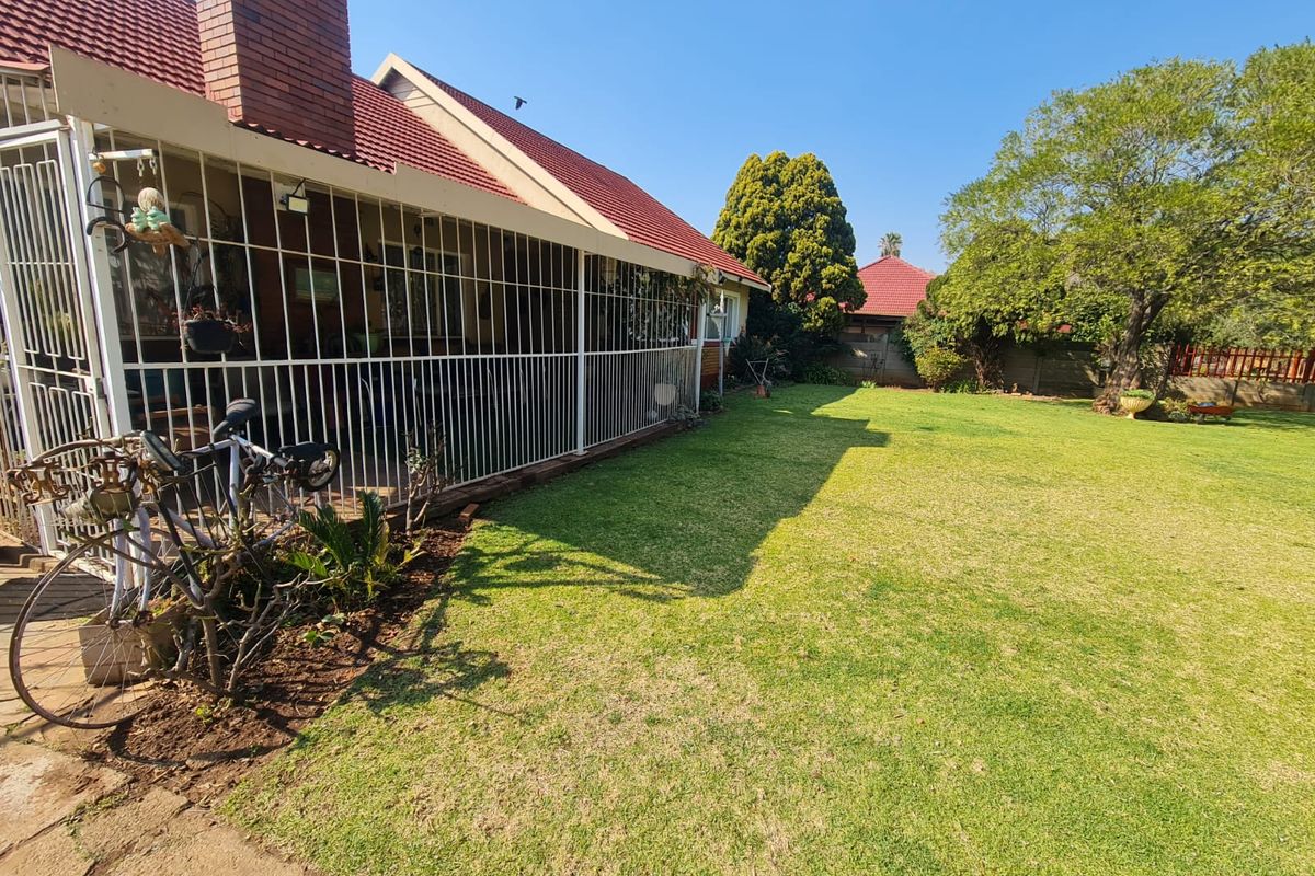 Rear view of the house featuring a covered patio area, brick chimney, and a spacious, well-maintained garden lawn.