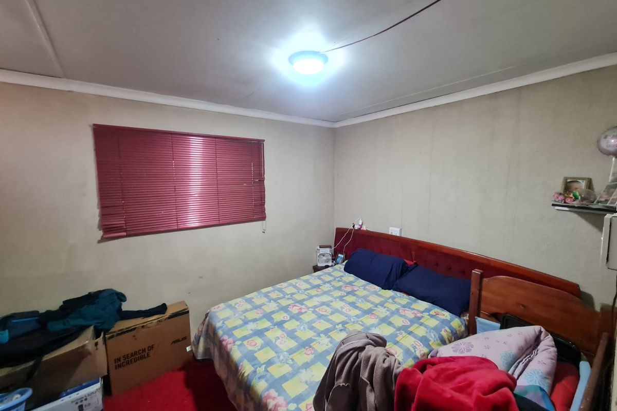 A bedroom featuring red carpeting, venetian blinds, and basic ceiling lighting. The room requires cosmetic updates to the wall finishes and general maintenance.
