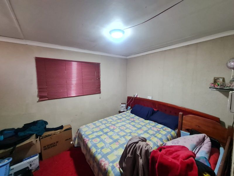 A bedroom featuring red carpeting, venetian blinds, and basic ceiling lighting. The room requires cosmetic updates to the wall finishes and general maintenance.
