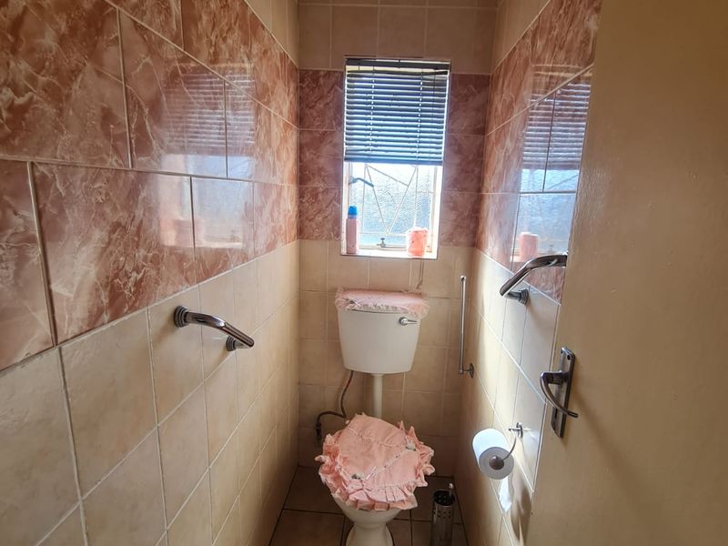 A compact bathroom featuring ceramic wall and floor tiles, a standard toilet, and installed grab rails for accessibility.