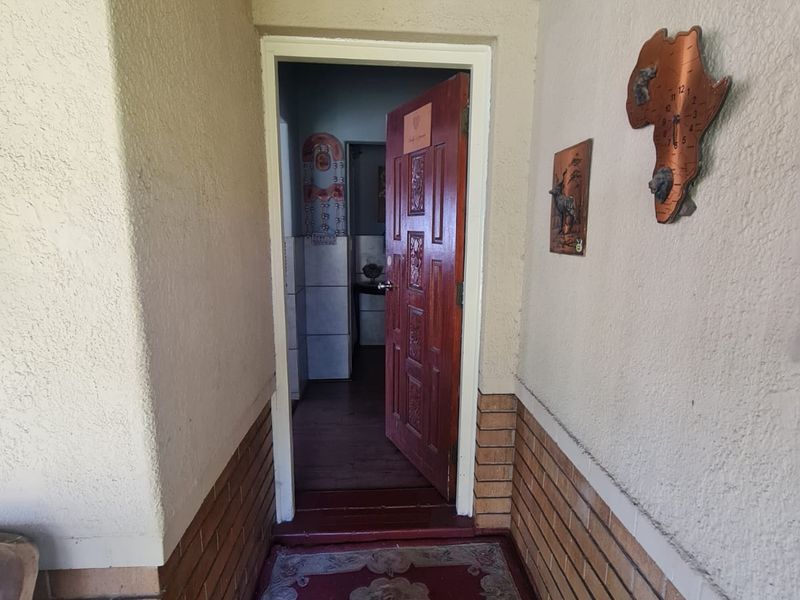 An entrance area featuring a solid wood door, brick baseboard detailing, and a ventilation grille, leading into the interior of the home.