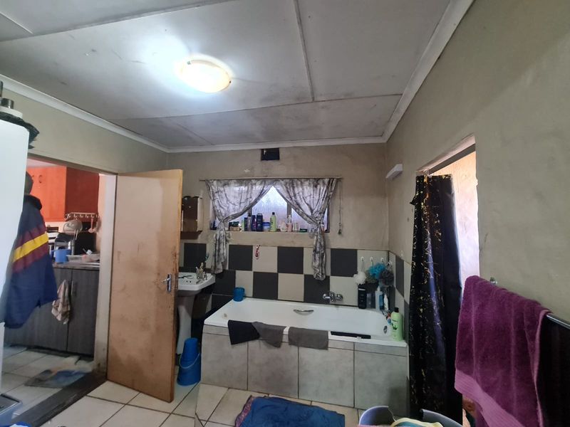 A dated bathroom featuring a built-in bathtub, pedestal basin, and tiled splashback, requiring cosmetic updates and ceiling repairs.