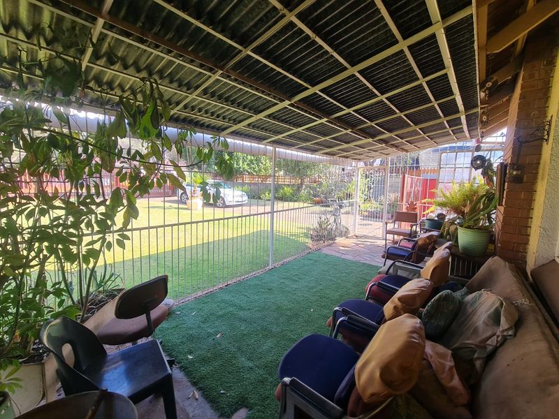 A covered outdoor patio area featuring a corrugated metal roof, metal security fencing, and artificial grass flooring, overlooking the garden.