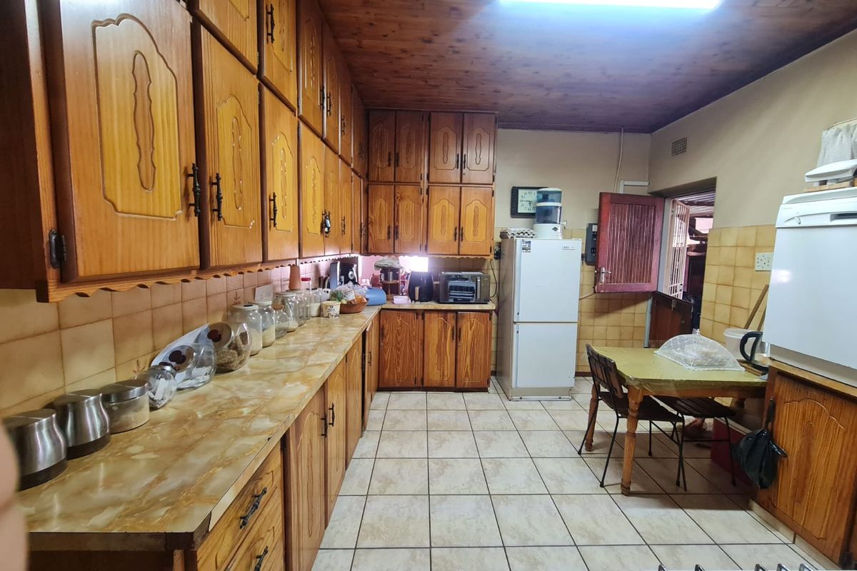 A traditional kitchen featuring extensive wooden cabinetry, laminate countertops, ceramic tile flooring, and a timber-paneled ceiling, offering a dated but functional layout.