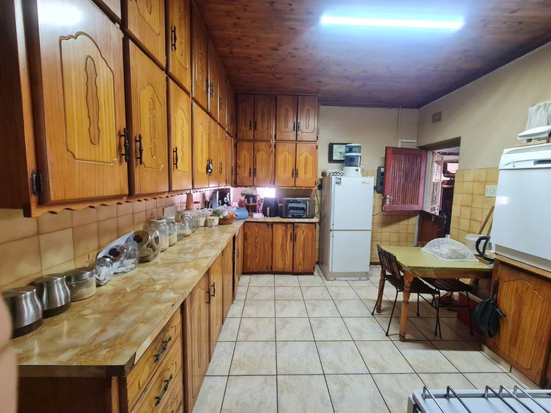A traditional kitchen featuring extensive wooden cabinetry, laminate countertops, ceramic tile flooring, and a timber-paneled ceiling, offering a dated but functional layout.