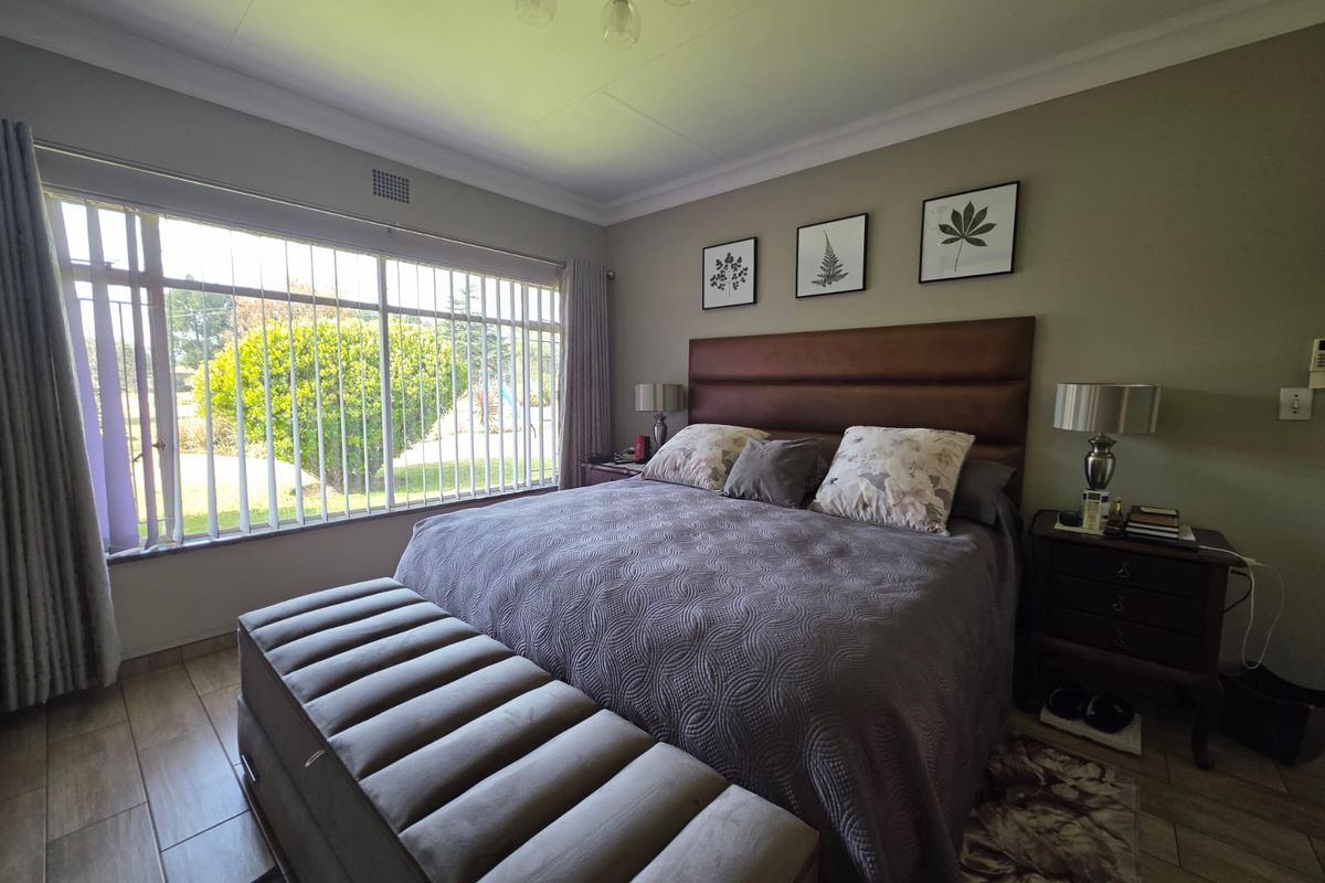 A well-maintained bedroom featuring tiled flooring, a large window with security bars, and neutral wall tones, providing a comfortable and functional living space.
