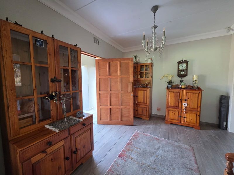 A living area featuring light-toned tiled flooring, coved ceilings, and a solid timber door leading to an adjacent space.