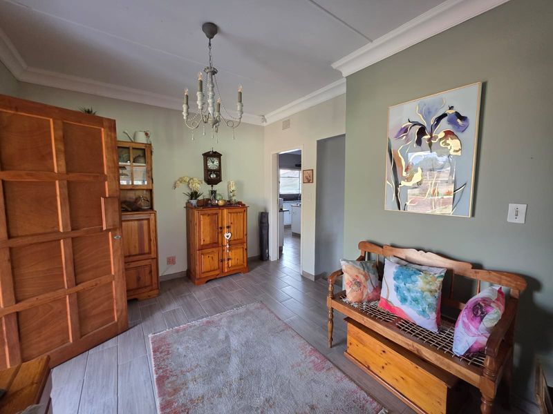 A well-maintained living area featuring tiled flooring, decorative ceiling cornicing, and a classic chandelier, with a view through to the kitchen area.