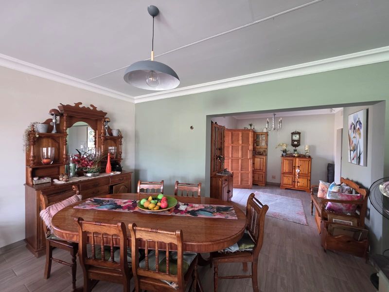 A dining room featuring tiled flooring, crown molding, and a central pendant light, with an open-plan flow into the adjacent living area.