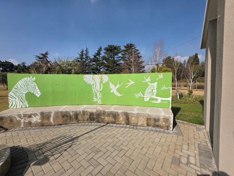 Outdoor paved patio area featuring a curved concrete bench with a decorative animal-themed mural wall.