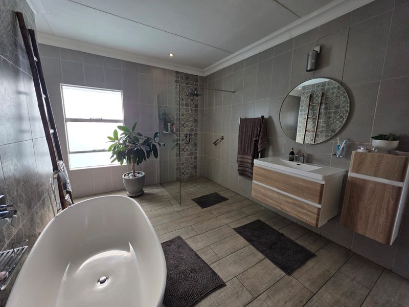 Modern bathroom featuring a freestanding bathtub, a spacious walk-in shower with decorative tile accents, and a contemporary wall-mounted vanity with ample storage.