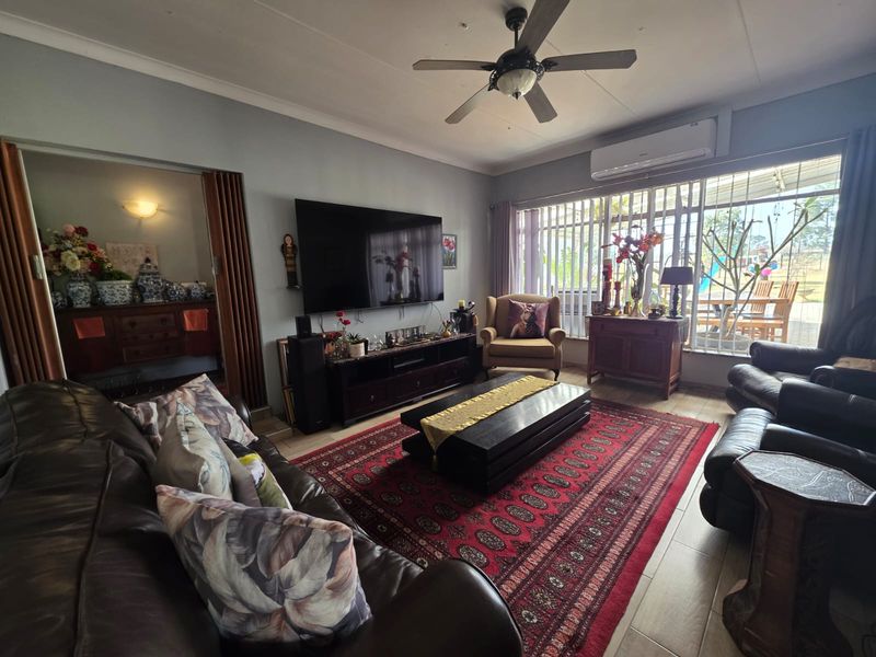 A comfortable living room featuring tiled flooring, a ceiling fan, and a wall-mounted air conditioning unit, with direct access to an outdoor patio area.