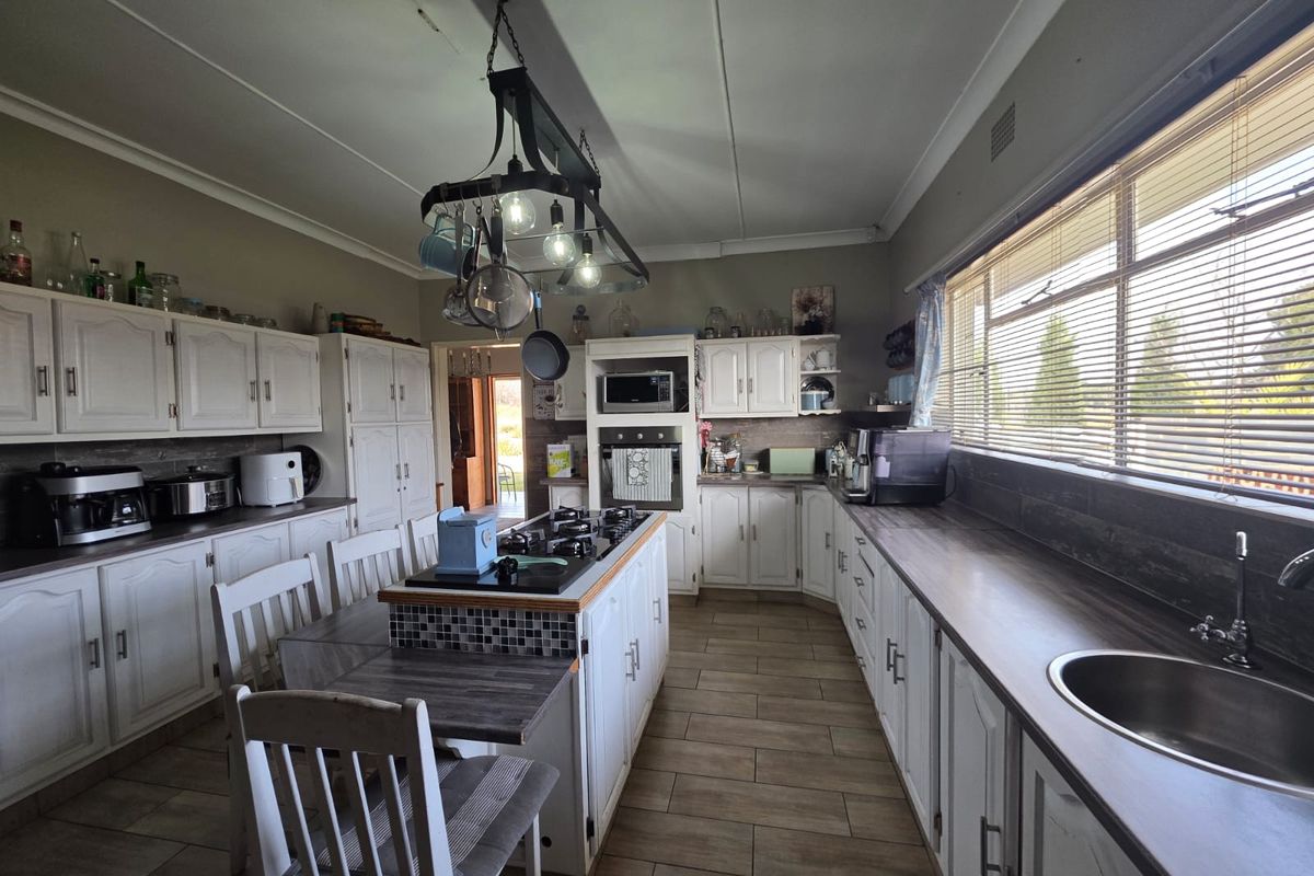 Spacious kitchen featuring white cabinetry, a central island with a gas hob, built-in oven, and ample counter space with a stainless steel sink.