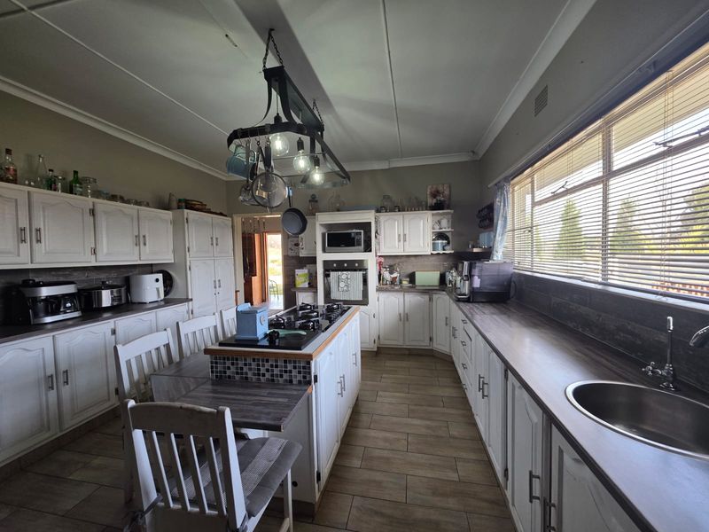 Spacious kitchen featuring white cabinetry, a central island with a gas hob, built-in oven, and ample counter space with a stainless steel sink.