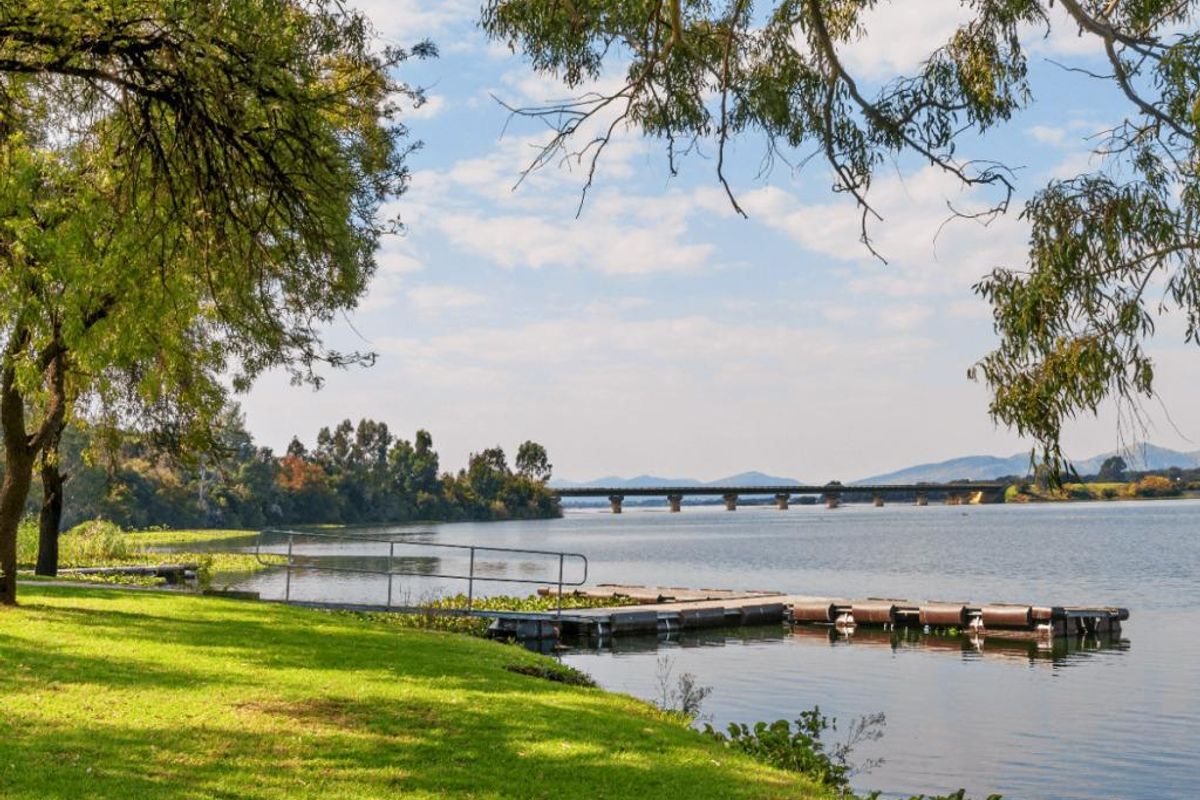 Scenic waterfront view featuring a floating jetty with a metal handrail, overlooking a calm lake with a bridge in the distance.