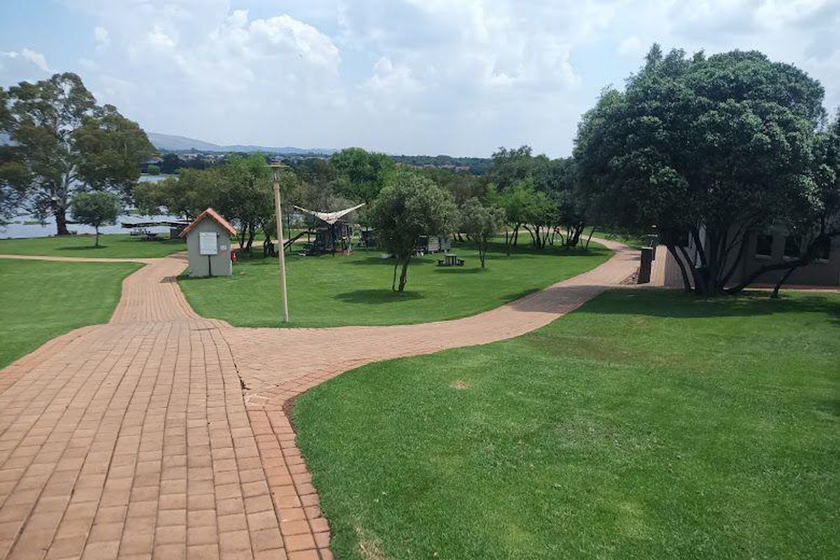 A well-maintained residential garden featuring paved walkways, expansive green lawns, and mature trees, offering a peaceful outdoor environment.