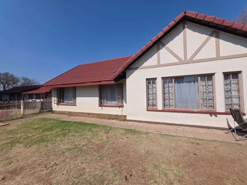 Rear view of a single-story house featuring a tiled roof, paved walkway, and metal-framed windows set against a lawn area.