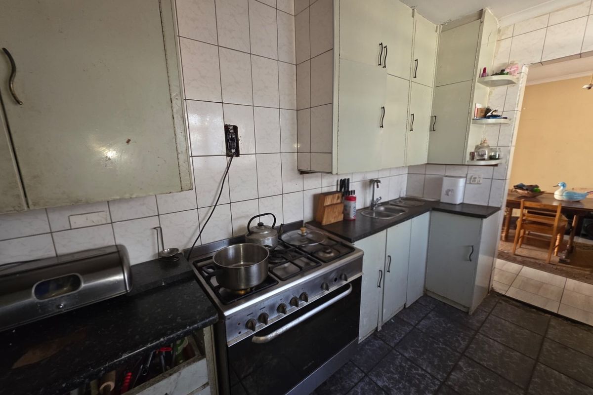A functional kitchen featuring built-in cabinetry, a gas stove with oven, and tiled surfaces, offering potential for modernization and aesthetic updates.