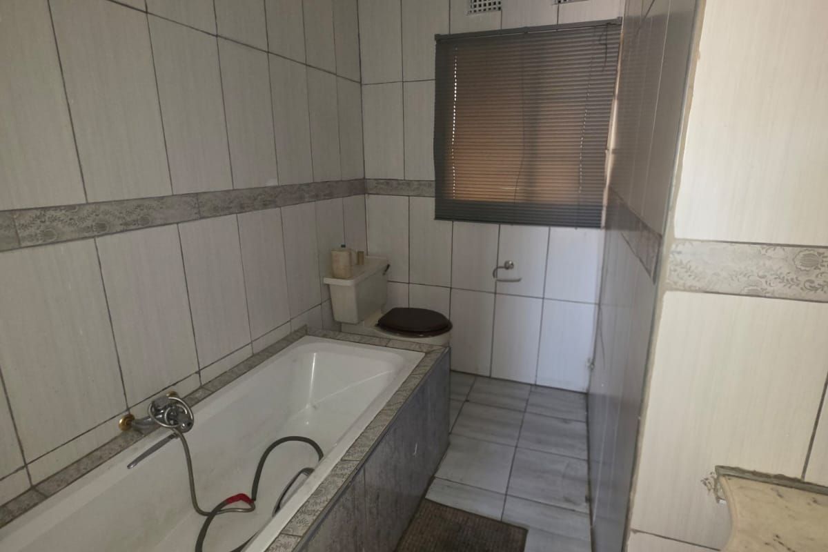 A dated bathroom featuring a bathtub, toilet, and vanity basin with full-height wall tiling and floor tiles.