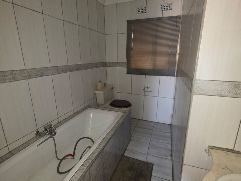 A dated bathroom featuring a bathtub, toilet, and vanity basin with full-height wall tiling and floor tiles.