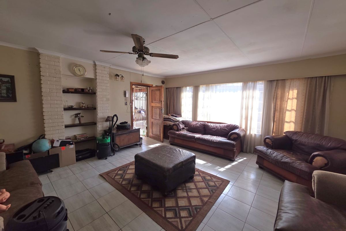 Spacious living room featuring tiled flooring, a brick fireplace surround with built-in shelving, and a ceiling fan, offering potential for modernization.