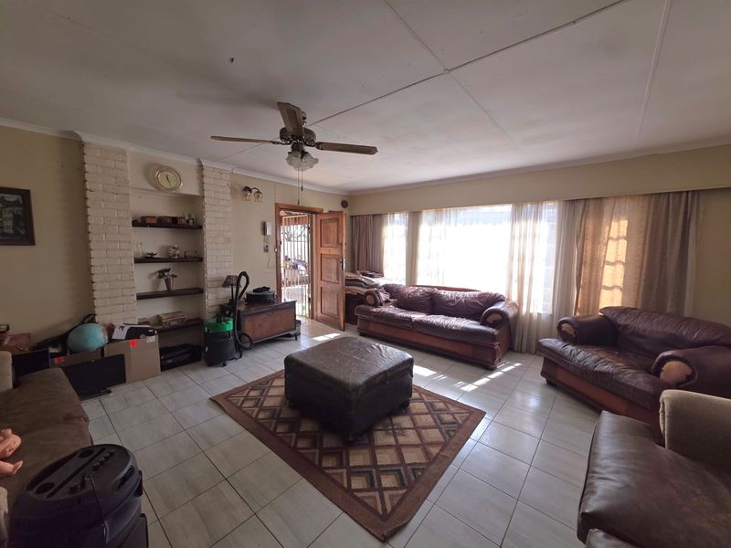 Spacious living room featuring tiled flooring, a brick fireplace surround with built-in shelving, and a ceiling fan, offering potential for modernization.