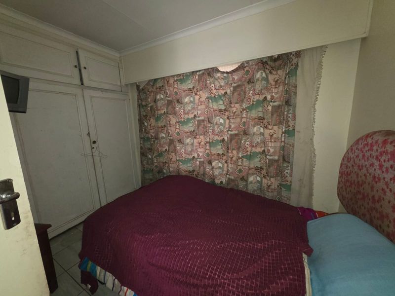 A bedroom featuring built-in cupboards, tiled flooring, and standard ceiling cornicing, currently requiring cosmetic updates to improve the overall aesthetic.