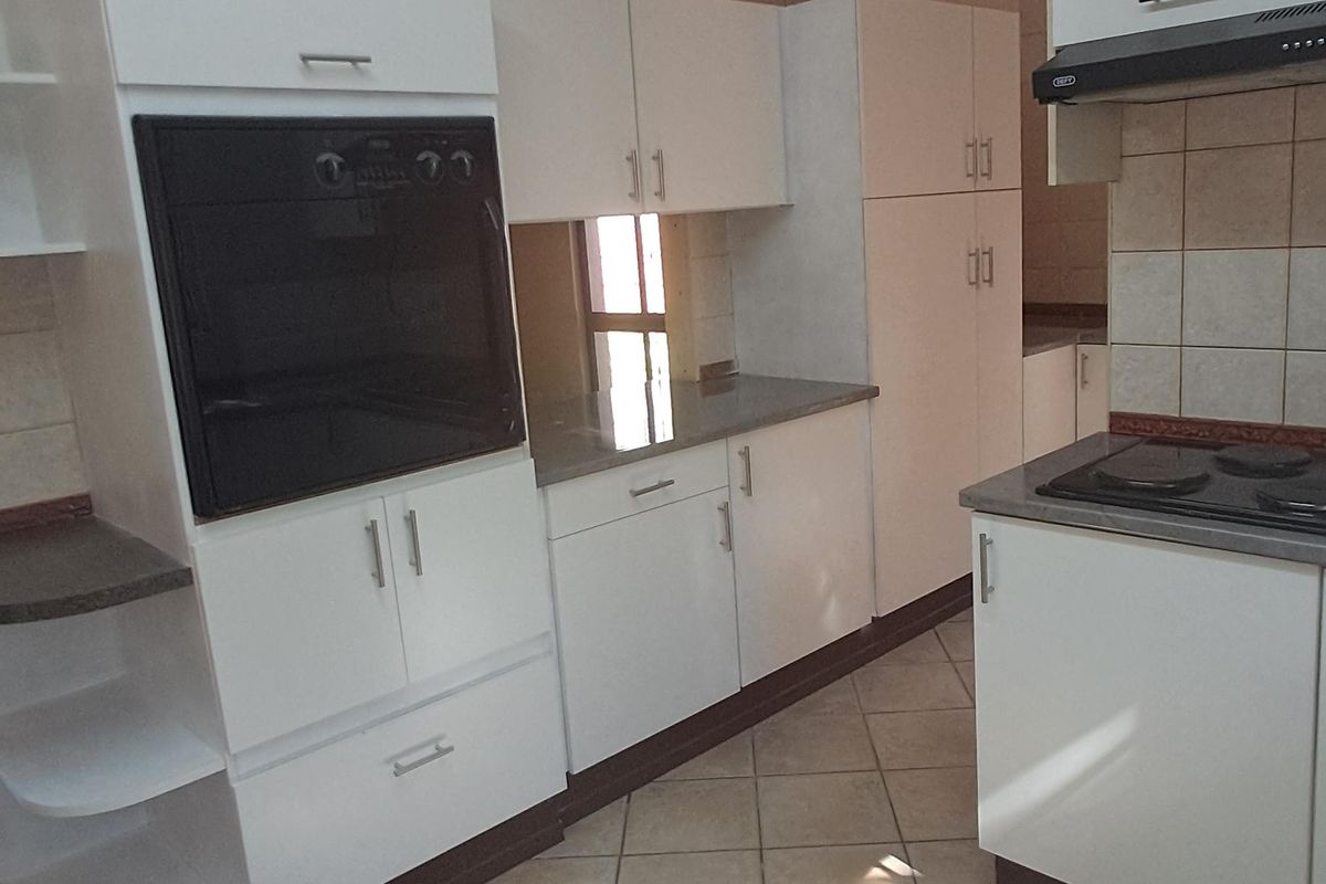A functional kitchen featuring white cabinetry, built-in oven, hob, extractor fan, and tiled flooring with a neutral backsplash.