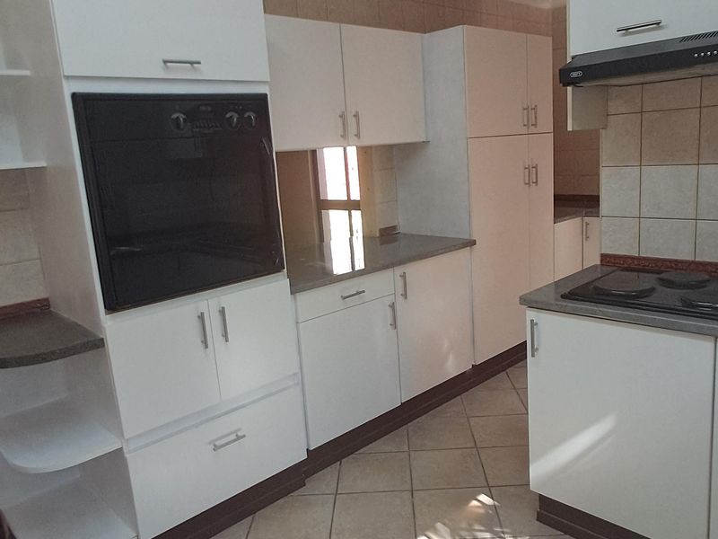 A functional kitchen featuring white cabinetry, built-in oven, hob, extractor fan, and tiled flooring with a neutral backsplash.
