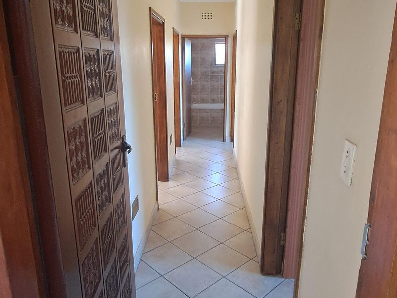 A functional hallway featuring tiled flooring and wooden door frames, providing access to multiple rooms including a bathroom at the end of the corridor.