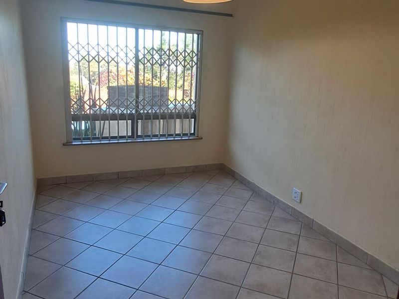 A clean, empty bedroom featuring neutral tiled flooring, a pendant light fixture, and a window fitted with a security gate.