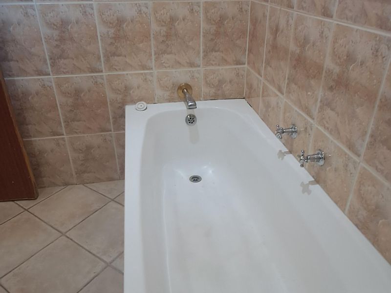 A functional bathroom featuring a built-in bathtub with wall-mounted chrome fixtures, complemented by neutral ceramic wall and floor tiling.