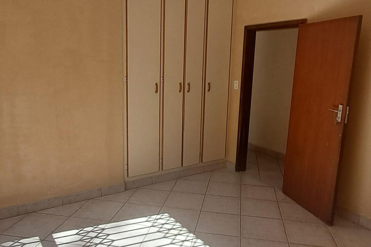 An empty bedroom featuring tiled flooring, built-in cupboards, and a security gate on the window, offering a blank canvas for potential updates.