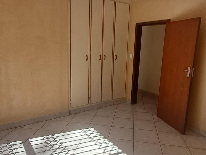 An empty bedroom featuring tiled flooring, built-in cupboards, and a security gate on the window, offering a blank canvas for potential updates.