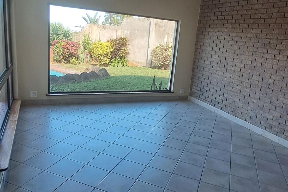 Spacious living area featuring a vaulted timber ceiling, a textured brick feature wall, and large windows overlooking the garden and pool area.
