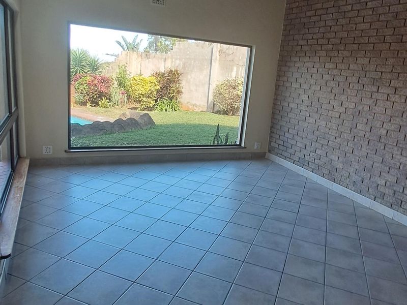 Spacious living area featuring a vaulted timber ceiling, a textured brick feature wall, and large windows overlooking the garden and pool area.