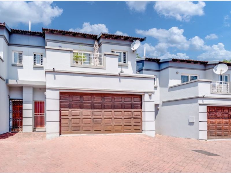 Front elevation of a townhouse complex featuring paved driveway access, double garages, and upper-level balconies with tiled roofing.