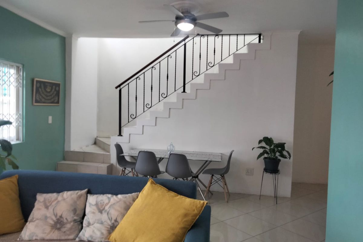 A living area featuring tiled flooring, a ceiling fan, and a staircase with a decorative wrought iron railing.