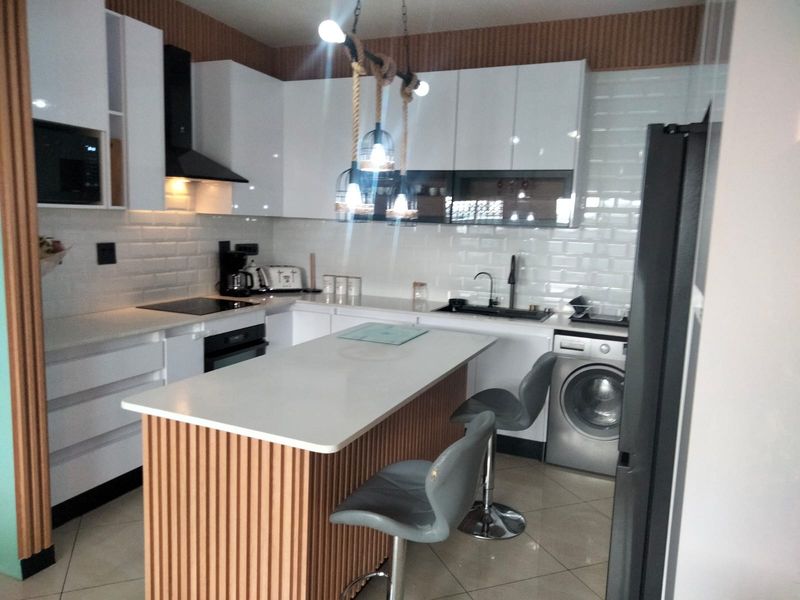 Modern kitchen featuring white gloss cabinetry, subway tile backsplash, a central island with slatted wood detailing, and integrated appliances.