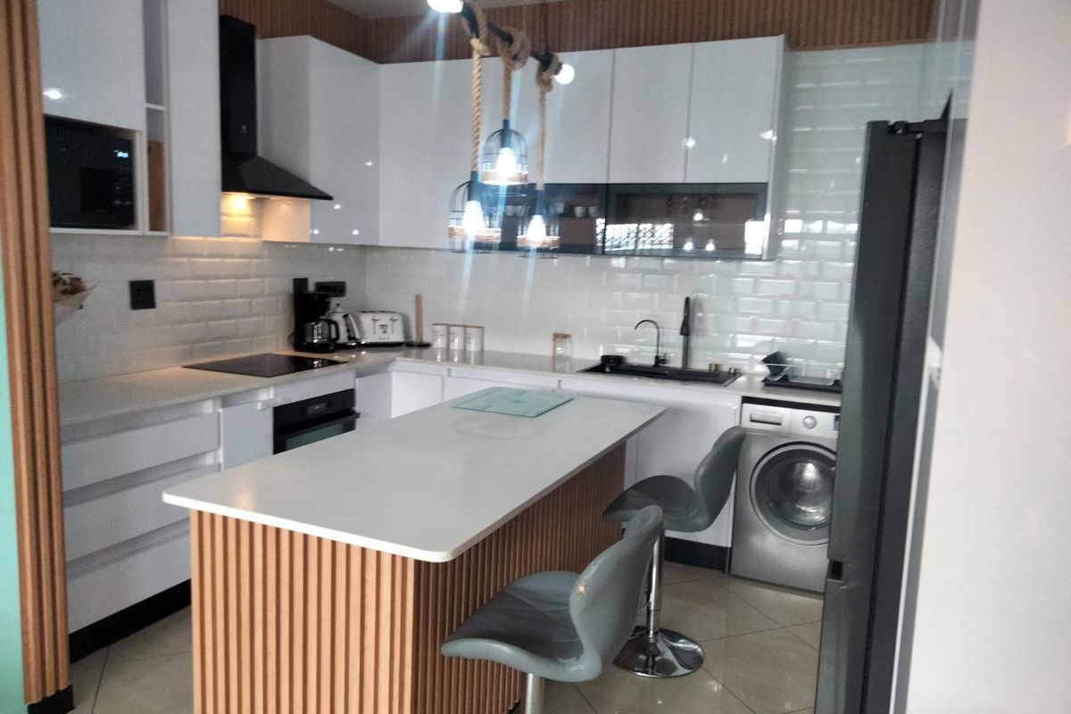 Modern kitchen featuring white gloss cabinetry, subway tile backsplash, a central island with slatted wood detailing, and integrated appliances.