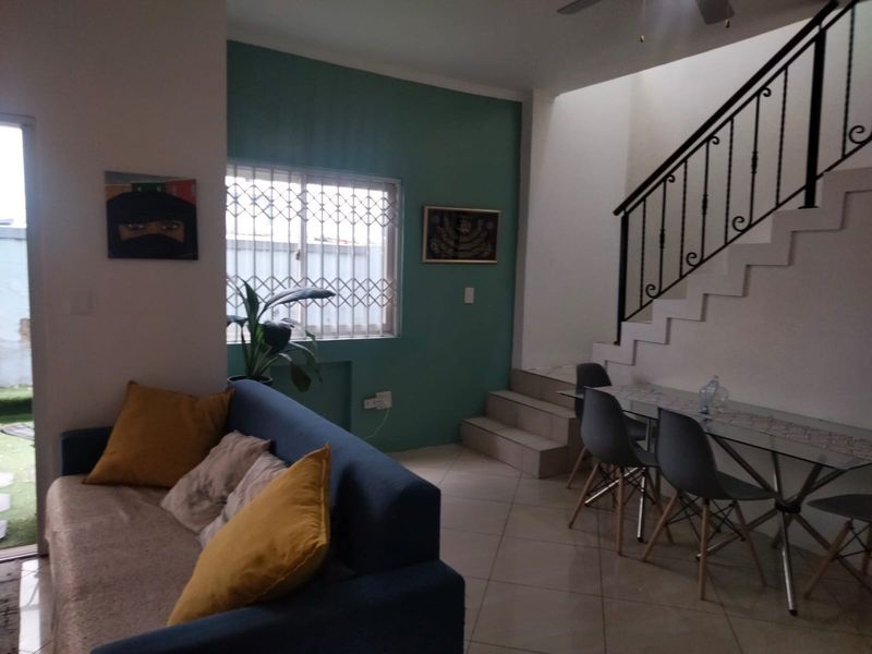 Open plan living and dining area featuring tiled flooring, a staircase with a wrought iron balustrade, and a security gate on the window.