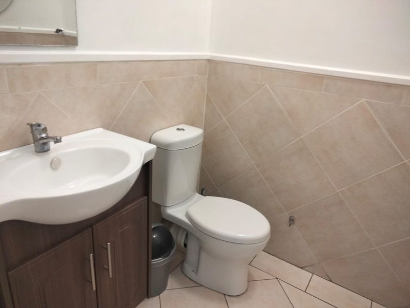 A functional bathroom featuring a vanity cabinet with basin, toilet, and neutral wall and floor tiling.