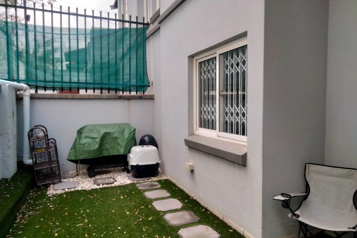 A compact rear courtyard featuring artificial turf, stone pavers, and a secure sliding window with a fitted security gate.