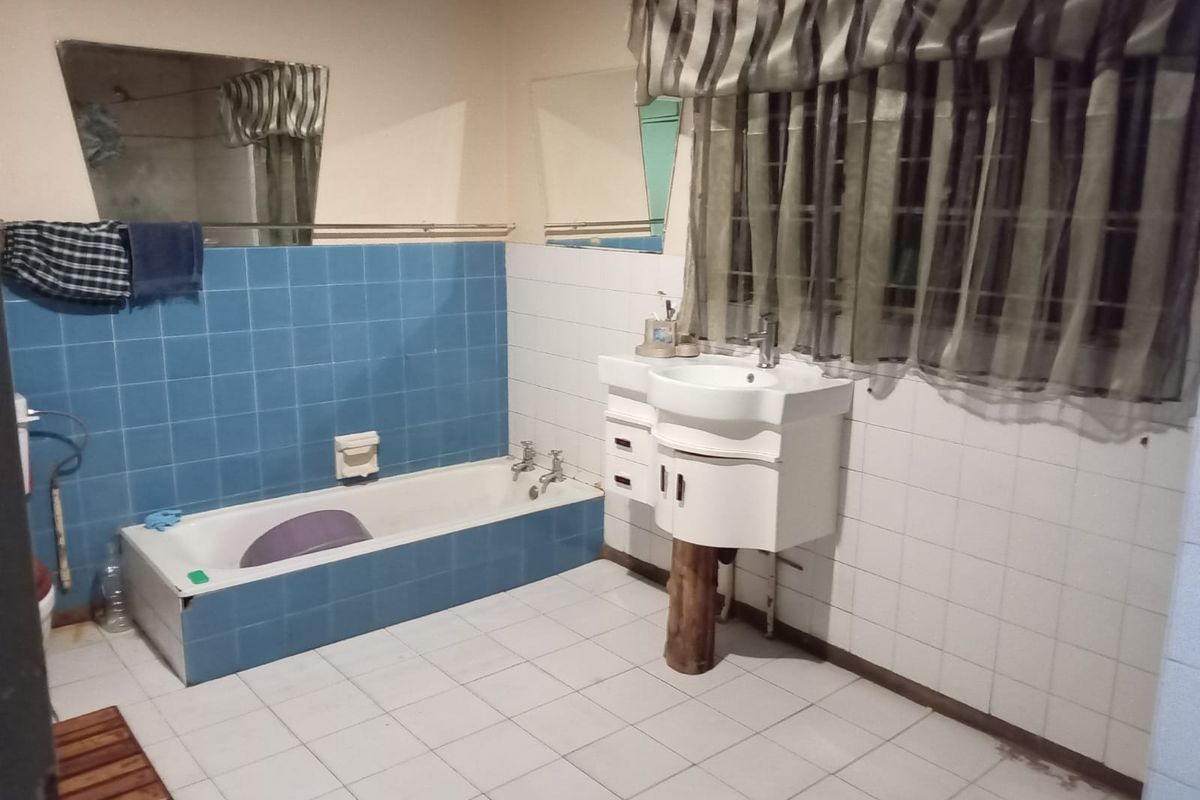 A dated bathroom featuring a built-in bathtub, pedestal vanity, and tiled finishes, offering potential for a modern renovation.