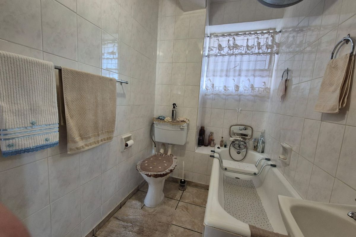 A functional bathroom featuring a bathtub, toilet, and basin with full-height wall tiling and tiled flooring.