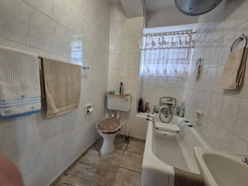 A functional bathroom featuring a bathtub, toilet, and basin with full-height wall tiling and tiled flooring.