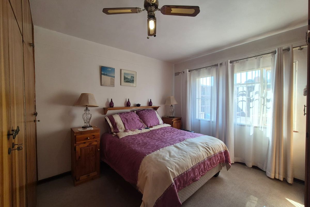 A well-maintained bedroom featuring built-in wooden cupboards, a ceiling fan, and large windows with security bars for added peace of mind.