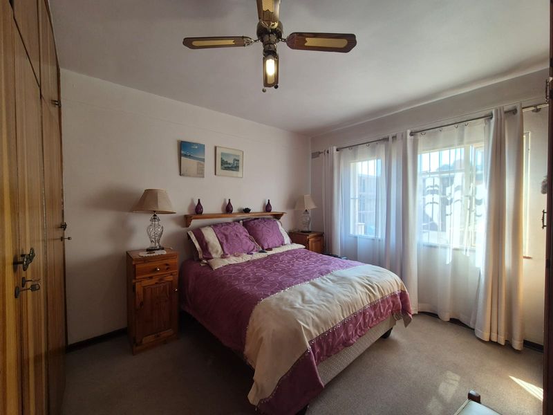 A well-maintained bedroom featuring built-in wooden cupboards, a ceiling fan, and large windows with security bars for added peace of mind.