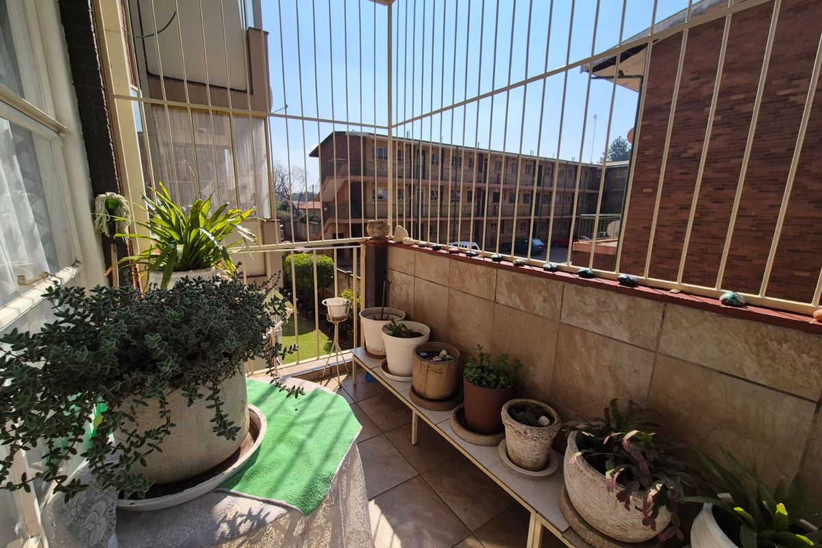 A balcony area featuring tiled flooring, tiled wall cladding, and protective metal security bars, overlooking the surrounding residential complex.